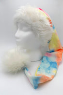 A colorful Santa-style hat with a fluffy white faux fur brim and large white pom-pom, displayed on a white mannequin head. The body of the hat features a tie-dye pattern in blue, orange, yellow, and pink shades.