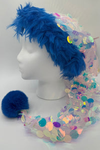 A Santa-style hat with bright blue faux fur trim, a long tail of iridescent pastel sequins, and a fluffy blue pom-pom displayed on a white mannequin head.