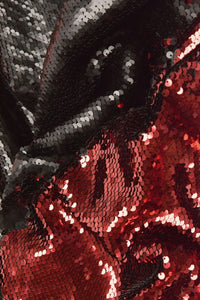 Close-up of reversible sequin fabric with red and black sequins, reflecting light to create a shiny, textured surface.