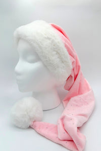 A soft pink Santa-style hat with scattered rhinestone embellishments, featuring a fluffy white faux fur brim and a large white pom-pom at the tip, displayed on a white mannequin head.
