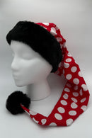 A mannequin head wearing a long red hat with large white polka dots, trimmed with black faux fur at the brim and a black pom-pom at the tip.