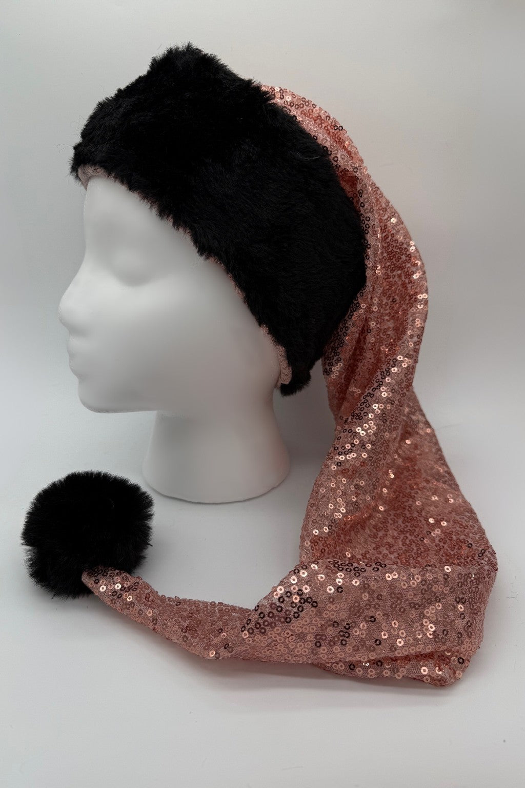 A mannequin head wearing a festive hat with a black faux fur brim and pom-pom, and a long, pointed body made of pink sequin fabric.
