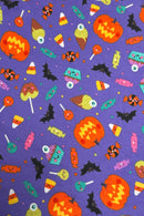 A playful Halloween-themed fabric pattern with a purple background featuring smiling jack-o’-lanterns, candy corn, lollipops, wrapped candies, cupcakes with eyepom-poms, bats, and ice cream cones, all illustrated in bright, cheerful colors with cute cartoon faces.