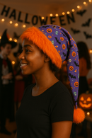 Right facing model, wearing a handmade purple Halloween hat with orange faux fur trim and a fluffy orange pom-pom, designed to drape and hang low.
