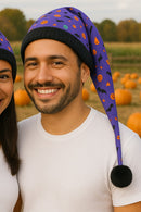 Two people wearing Halloween-themed hats with pumpkins and bats in a pumpkin patch.