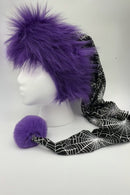 Mannequin head wearing a long festive hat with bright purple faux fur around the crown, a black fabric tail patterned with white spiderwebs, and a matching fluffy purple pom-pom at the end. The hat is displayed against a plain white background with reflective panels on the sides.