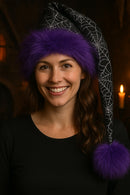Woman wearing a spiderweb hat with a purple pom-pom against a dark background
