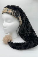 A mannequin head wearing a long black panne Velvet hat with a Burberry fabric band, large black button detail, and a fluffy beige pom-pom at the end.