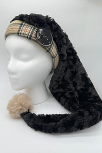 A mannequin head wearing a long black panne Velvet hat with a Burberry fabric band, large black button detail, and a fluffy beige pom-pom at the end.