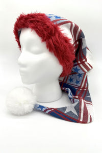 A mannequin head wearing a long festive hat with a red faux fur trim, patterned fabric in red, white, and blue with stars and stripes, and a large fluffy white pom-pom at the end.