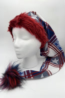 A mannequin head wearing a long festive hat with a red faux fur trim, patterned with blue, white, and red plaid and star designs. The hat has a large fluffy pom-pom at the end in shades of red, blue, and black.