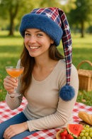 Adult wearing a handmade red, white, and blue plaid holiday hat with stars, trimmed with steel blue faux fur and a matching pom, at a picnic scene.