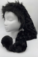 A black panne Velvet  hat with a long tail ending in a large fluffy black trim and pom-pom, displayed on a white mannequin head against a plain white background.