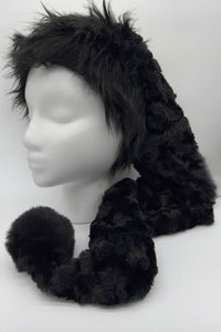A black panne Velvet  hat with a long tail ending in a large fluffy black trim and pom-pom, displayed on a white mannequin head against a plain white background.