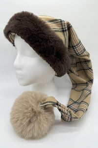 Burberry plaid winter hat with a brown faux fur trim and a long tail ending in a large beige fluffy pom-pom, displayed on a white mannequin head against a plain background.