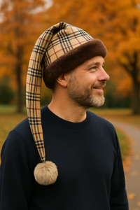 Man wearing a handmade Burberry plaid hat with brown faux fur trim and a tan pom-pom that hangs about 8 inches below his shoulder, standing outdoors in autumn.